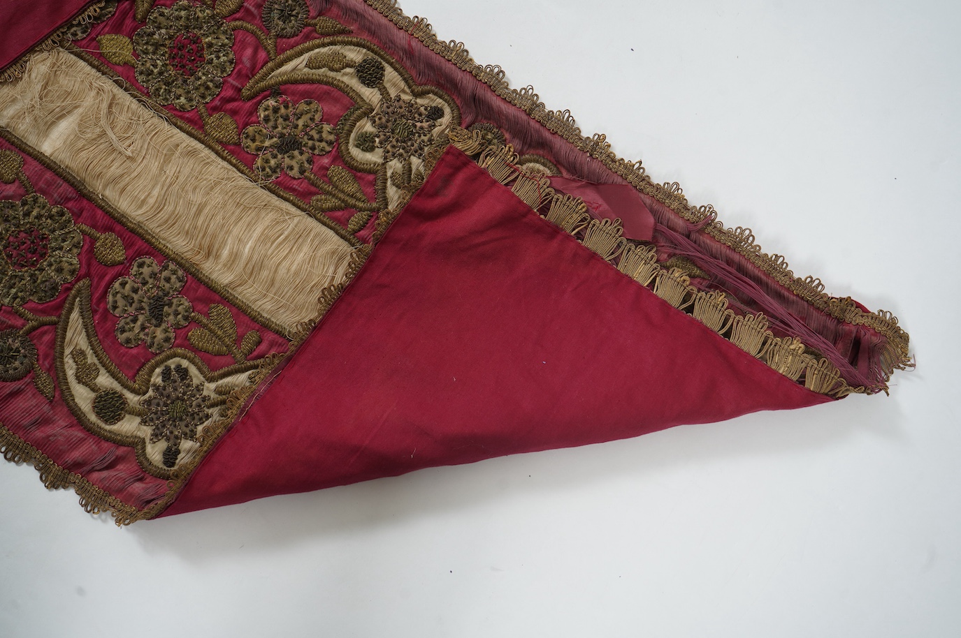 A 19th century Indian red and cream silk runner, heavily embroidered with scrolling motifs, using a variety of stump work and gold wire work stitches, with earlier Mughal influences, 118cm x 46.5cm (not including braid),